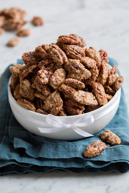 Soft candied pecans in  a white bowl with a blue napkin, made fresh to order.